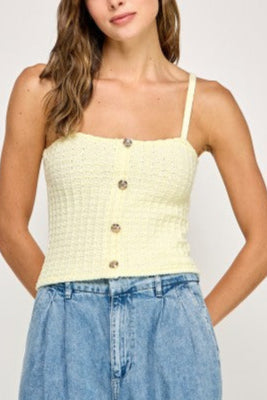 Woman wearing a light yellow textured tank top with button details on a plain background